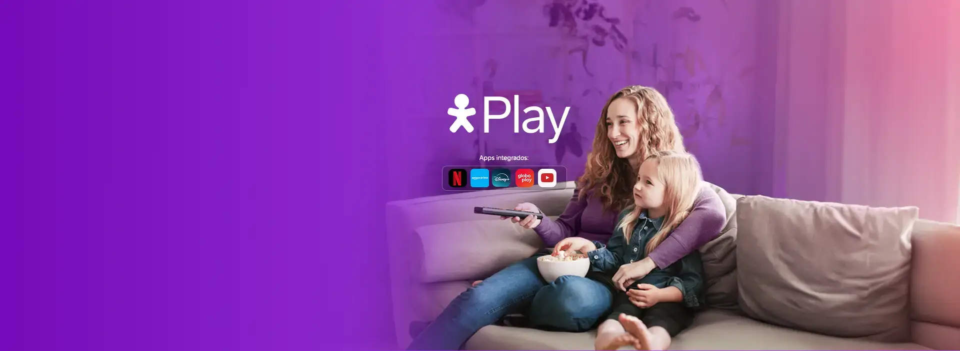 Imagem de uma mãe e filha, sentadas no sofá, comendo pipoca e sorrindo.